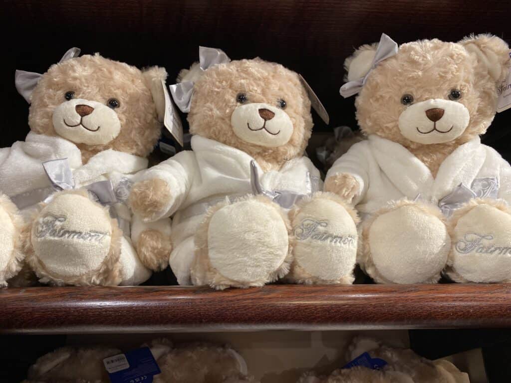 Three light brown Teddy bears wearing white bathrobes and bow in hair sitting on a wooden shelf in the Canadian Pacific shop at Fairmont Banff Springs.