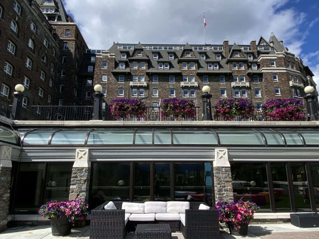 Exterior of Fairmont Banff Springs with baskets of pink flowers and seating area.