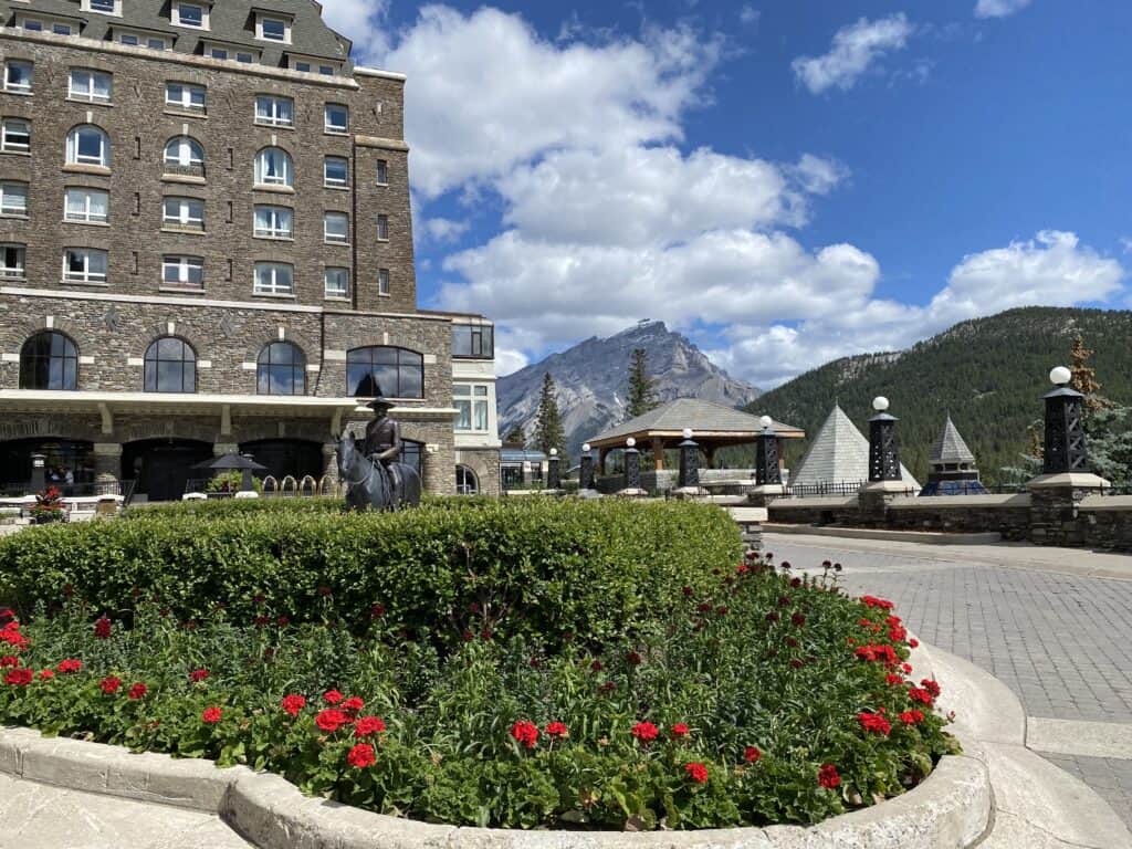Grounds of the Fairmont Banff Springs Hotel - gardens in foreground with mountie statue, hotel building behind and mountains in background.
