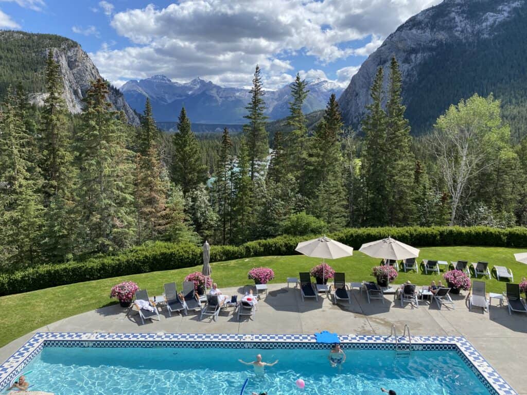 Outdoor pool and seating area at Banff Springs Hotel with mountains in background.