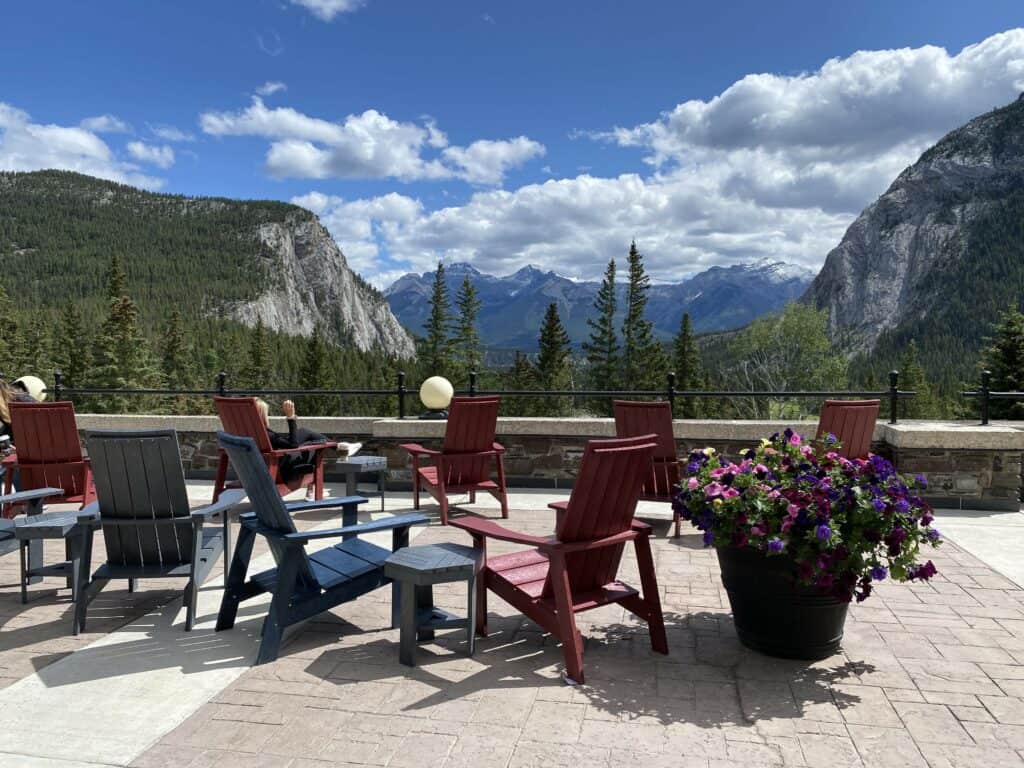 Several chairs and tables beside flower planter with trees and mountains in background.