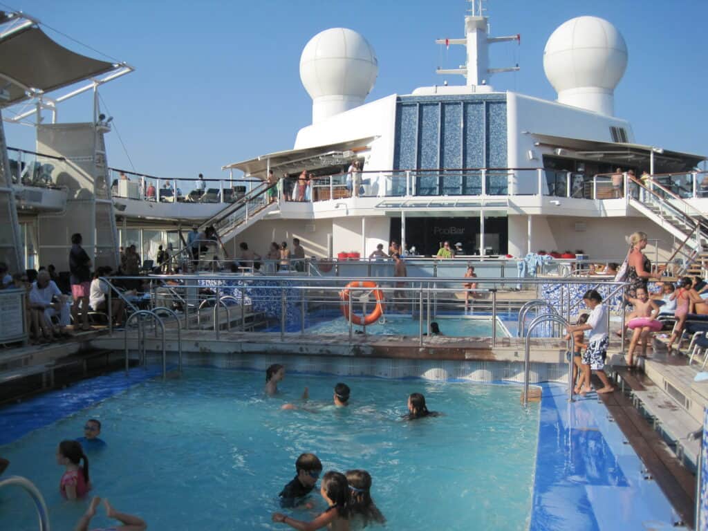 Passengers in pool and around deck on Celebrity Equinox with blue sky.
