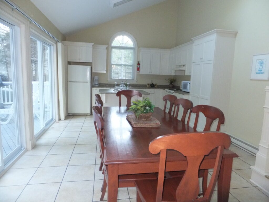 White kitchen with long wooden dining table - glass patio doors at left - 3 bedroom cottage kitchen at Kindred Spirits, Cavendish, Prince Edward Island.