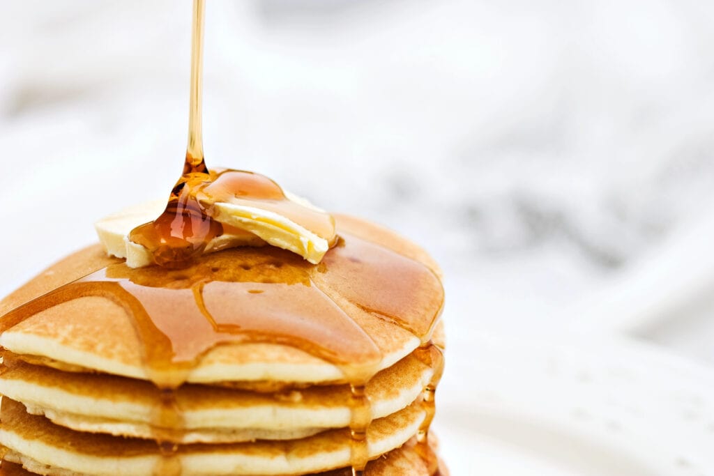 Stack of pancakes topped with butter and maple syrup with white background.