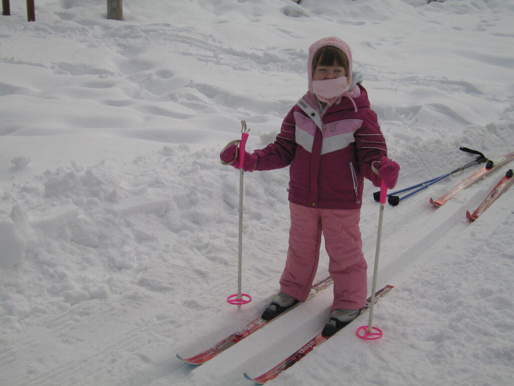 Young girl dressed in pink ski suit, pink hat and scarf on skis and holding ski poles in snow on cross country ski trail at Chateau Montebello.