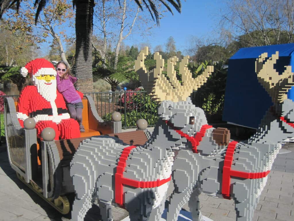 Young girl sitting with Lego creation of Santa Claus in sleigh with two reindeer.