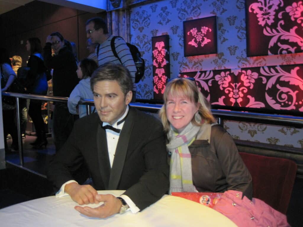 Woman sitting at table with "George Clooney" wax figure at Madame Tussauds in London.