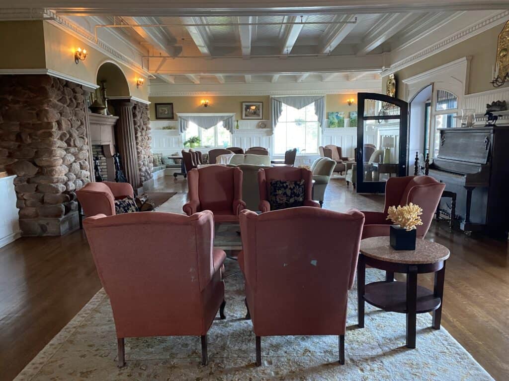 Sitting areas on main level of Dalvay-by-the-Sea with highbacked rose coloured chairs, large stone fireplace and piano.