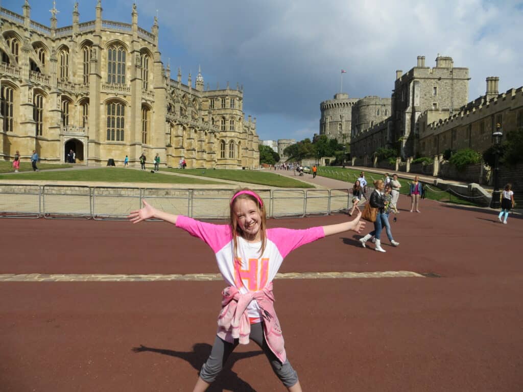 Smiling young girl in pink and white top with arms outstretched in front of Windsor Castle.