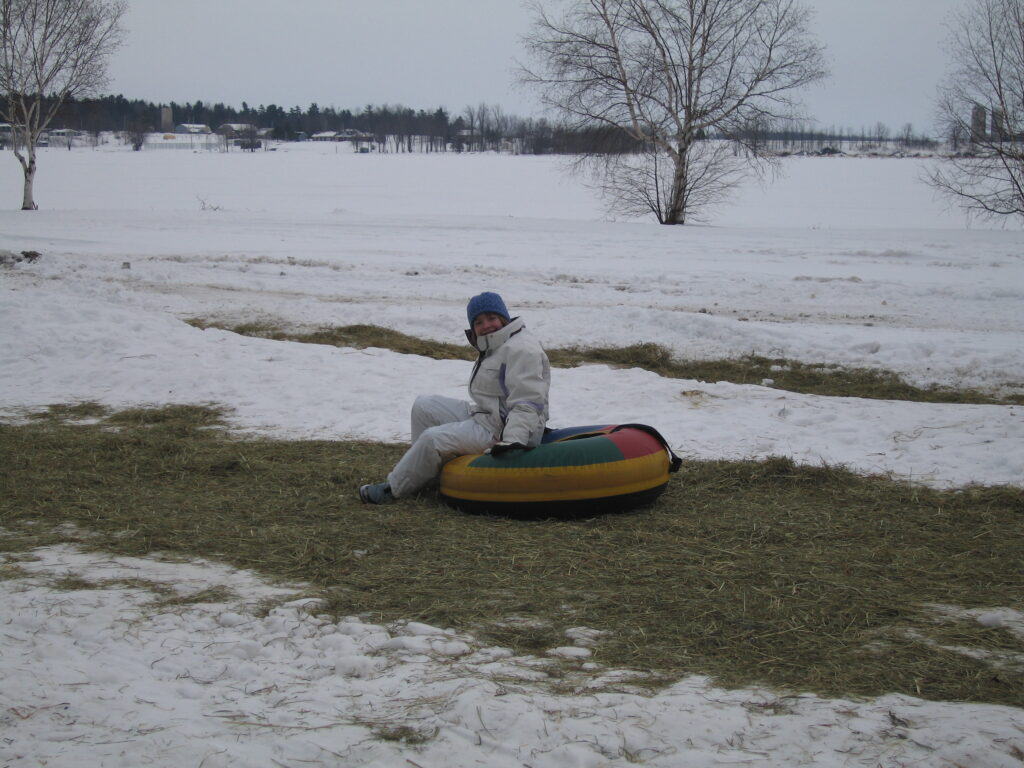 Young girl in white ski suit sitting on tube - straw on top of snow.