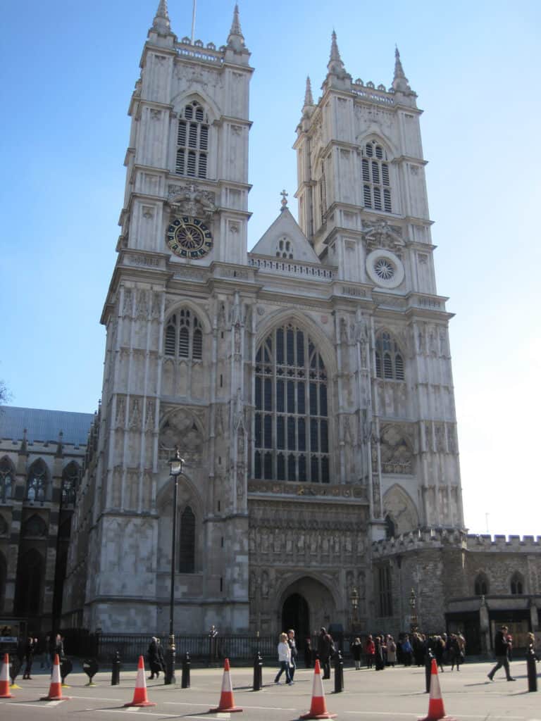 People walking in front of Westminster Abbey, London on a clear day with blue sky.