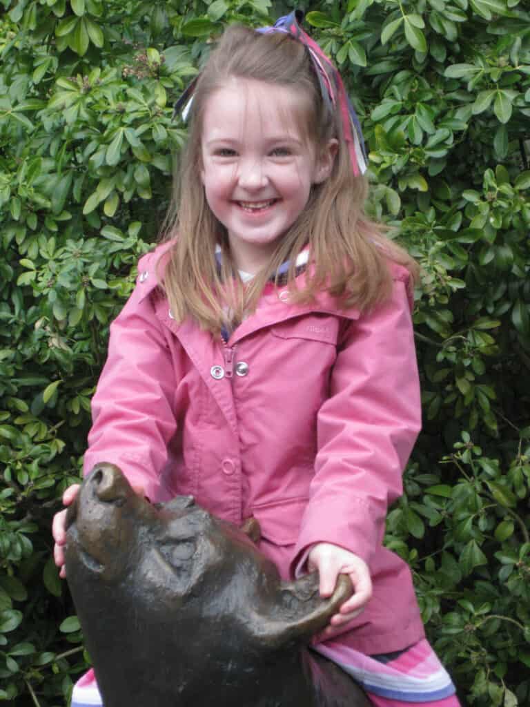 Young girl in pink coat playing on Winnie the Pooh statue at the London Zoo.