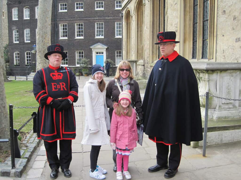 Woman, teen girl and young girl standing with beefeaters at the Tower of London.