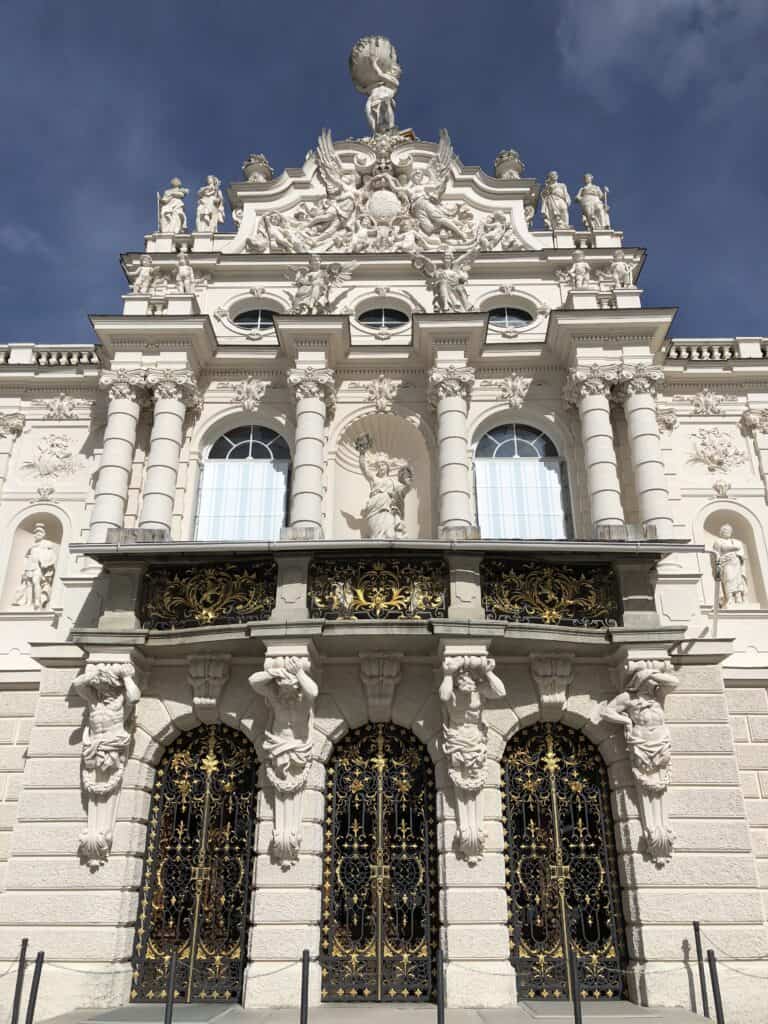 White exterior of Linderhof Palace against bright blue sky.