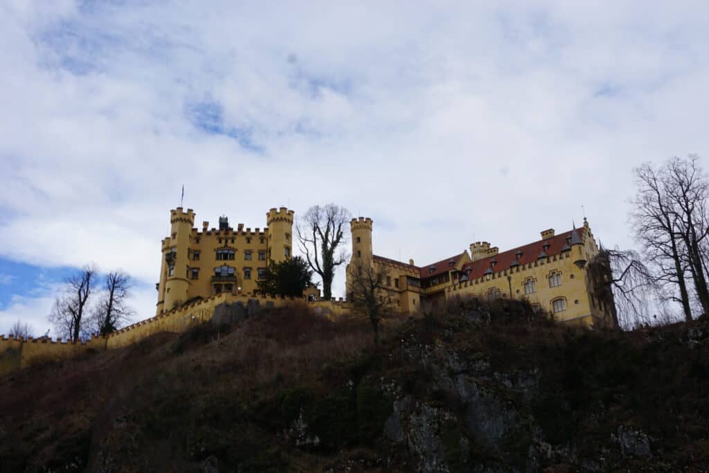 Exterior of Hohenschwangau Castle - mustard coloured castle set atop a hill.