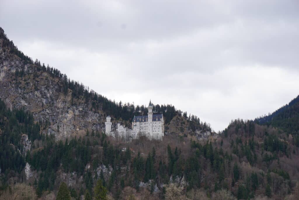 View of Neuschwanstein Castle from the distance with late winter gray cloudy sky.