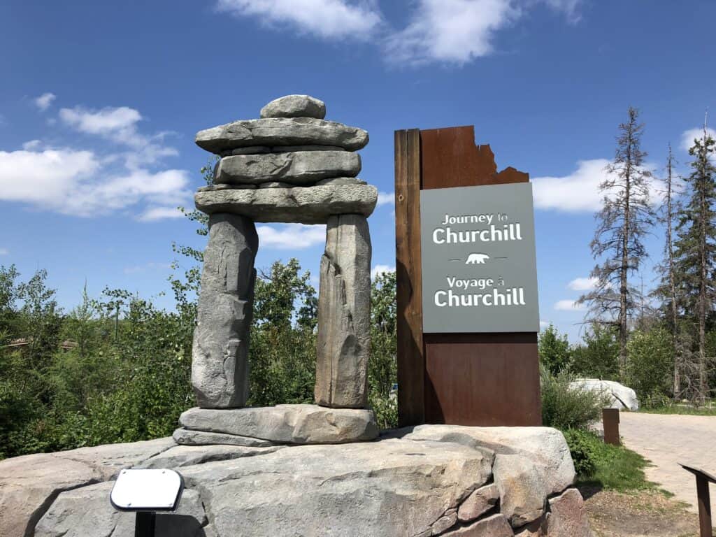 Large inukshuk and sign reading Journey to Churchill on rock platform at Assiniboine Park Zoo in Winnipeg, Manitoba.