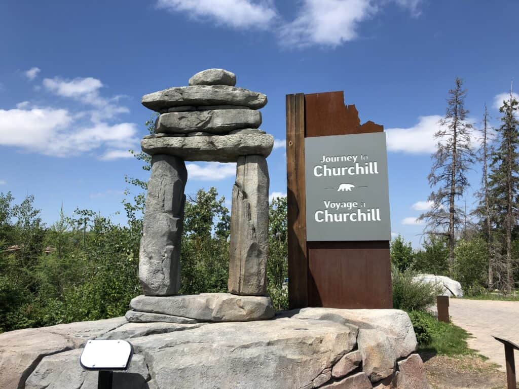 Large inukshuk and sign reading Journey to Churchill on rock platform at Assiniboine Park Zoo in Winnipeg, Manitoba.
