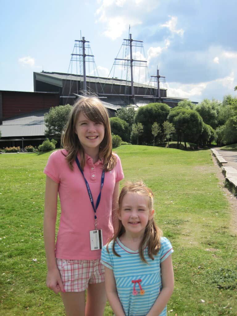 Two young girls standing in Stockholm with sails of the Vasa Museum in the background.