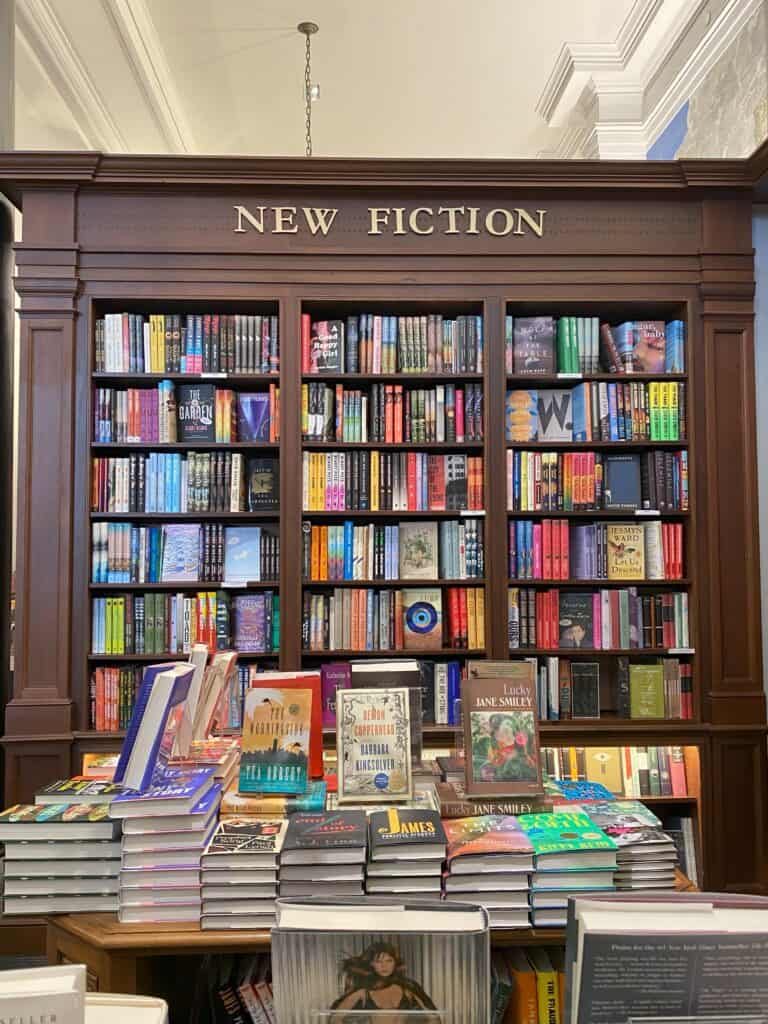 Dark wooden shelves of books below New Fiction and table of books on display at Rizzoli Bookstore in New York City.