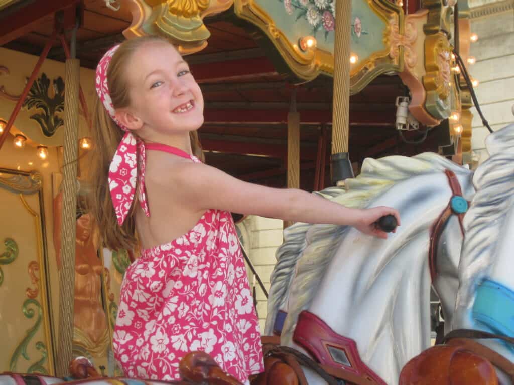 Young girl in bright pink and white flowered top riding on a horse on a carousel in Avignon, France.