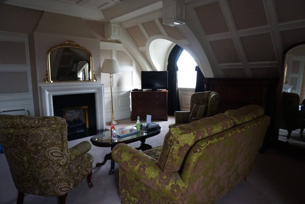 Killarney Park Hotel O'Connell suite seating area - panelled woodwork and curved window, fireplace with mirror and green and brown flowered chairs, small tv on stand by window.