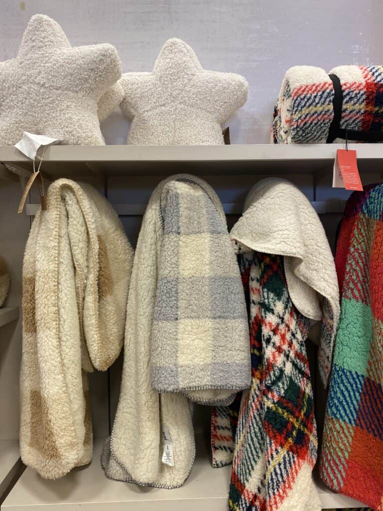Display of cozy reading blankets hanging at an Indigo shop - brown and cream check, grey and cream check and red and green plaids.