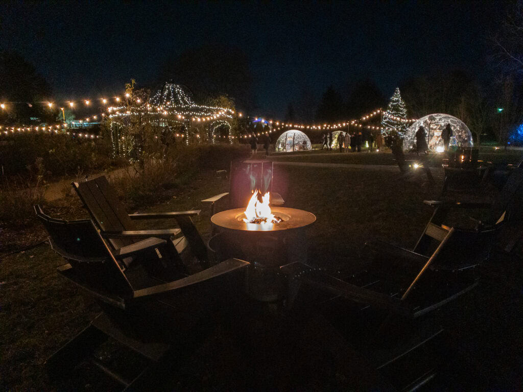 Chairs around a firepit with lights of Hendrie Park in the background at Winter Wonders, Royal Botanical Garden.