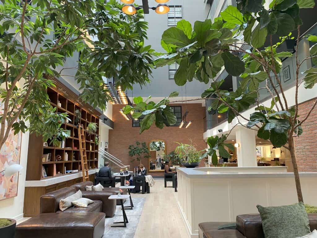 Lobby of the Metcalfe Hotel with bookcases and ladder, people sitting at tables and greenery.