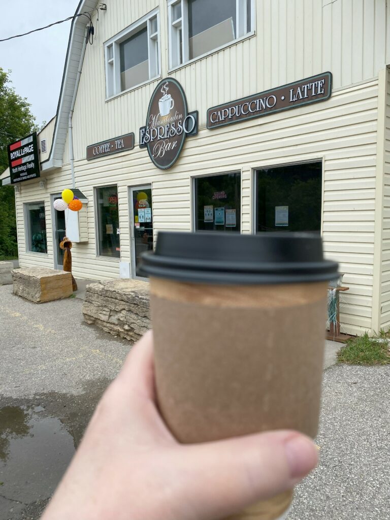 hand holding take-out coffee cup in front of Netti's Manitoulin Espresso Bar in Mindemoya on Manitoulin Island.