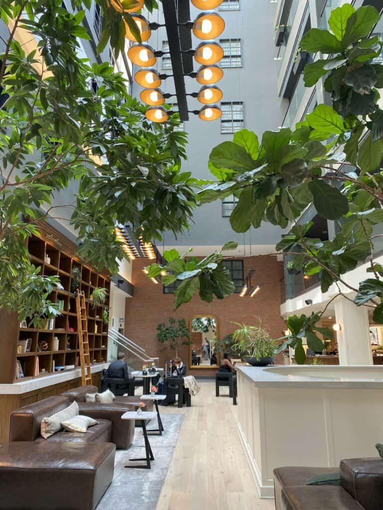 Cozy llobby of The Metcalfe Hotel in Ottawa - brown leather chairs with cream coloured pillows, white/black tables, library shelves with ladder, greenery.