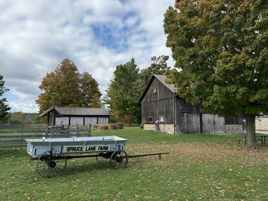 Light blue wagon with Spruce Lane Farm in black lettering in foreground and trees and barns in background.