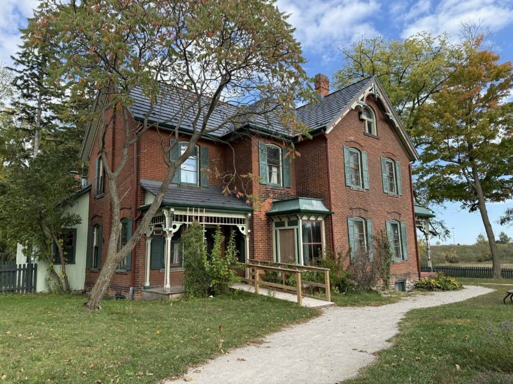 red brick farmhouse with porch and wheelchair ramp, dark shutters and roof.