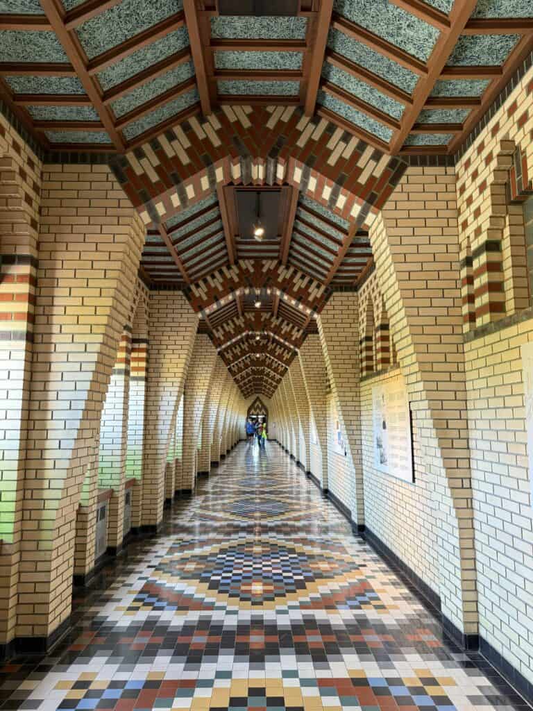 interior hallway of Abbey de Saint-Benoit-du-Lac - sand coloured brick walls and arches with colourful mosaic floor pattern and ceiling.