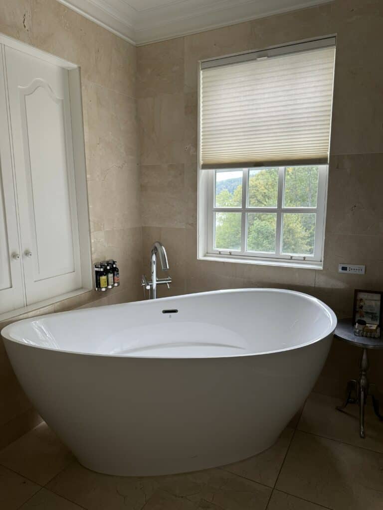 large freestanding white bathtub in front of window in room at Manoir Hovey, North Hatley, Quebec.