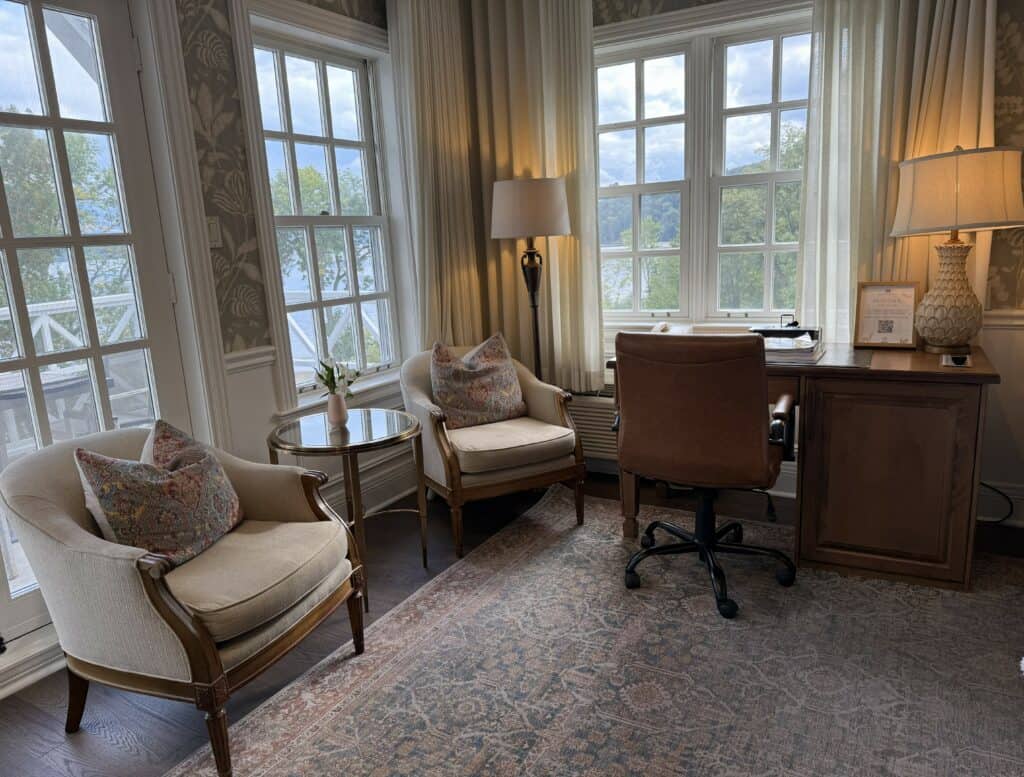 seating area in room at Manoir Hovey with two light brown coloured upholstered chairs with pillows in front of windows and desk with chair.