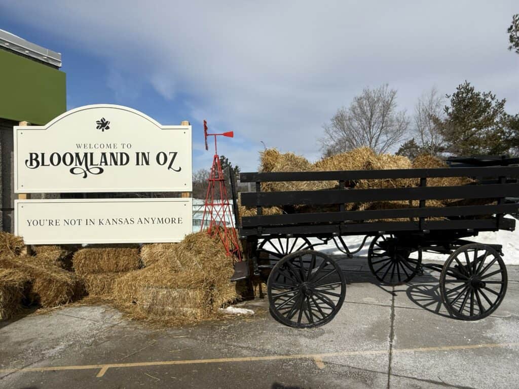 black wagon, hay bales and red windmill at entrance to royal botanical gardens in burlington, ontario with sign reading "Welcome to Bloomland in Oz - You're not in Kansas anymore".