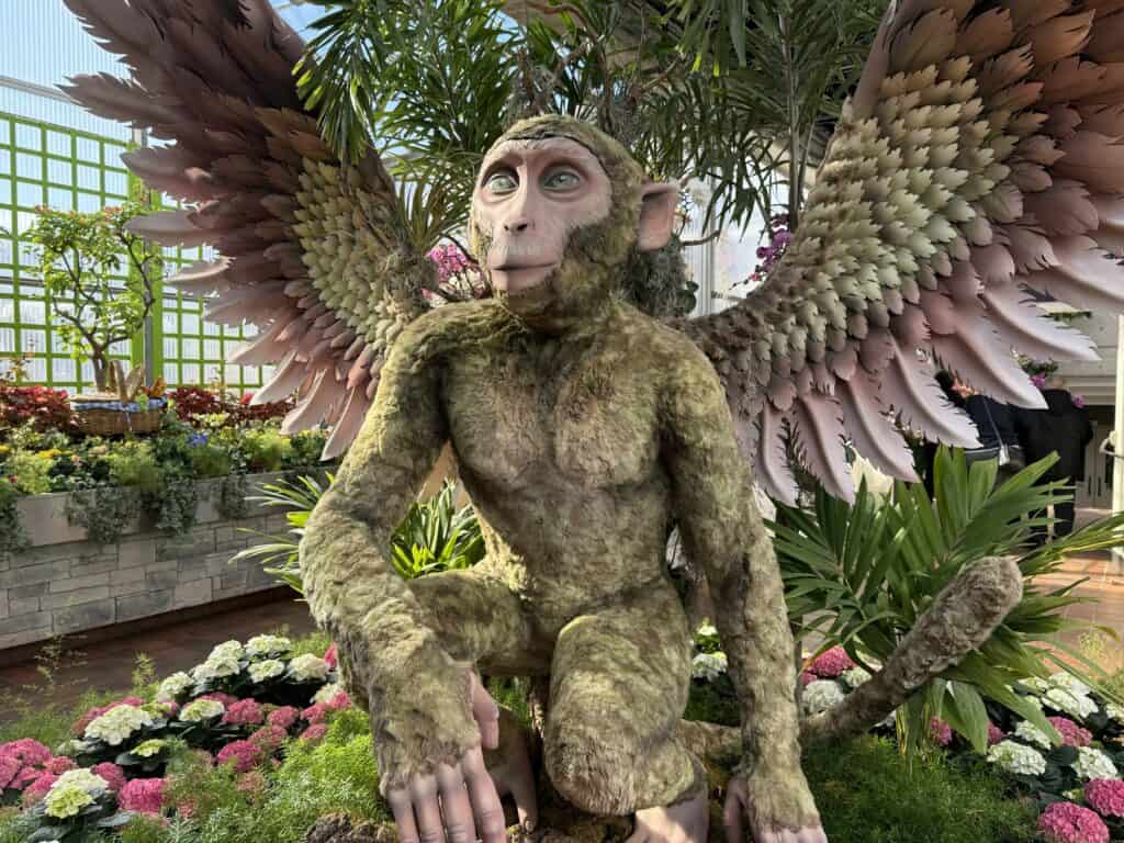 flying monkey on display amidst flowers and plants in breezeway at royal botanical gardens.