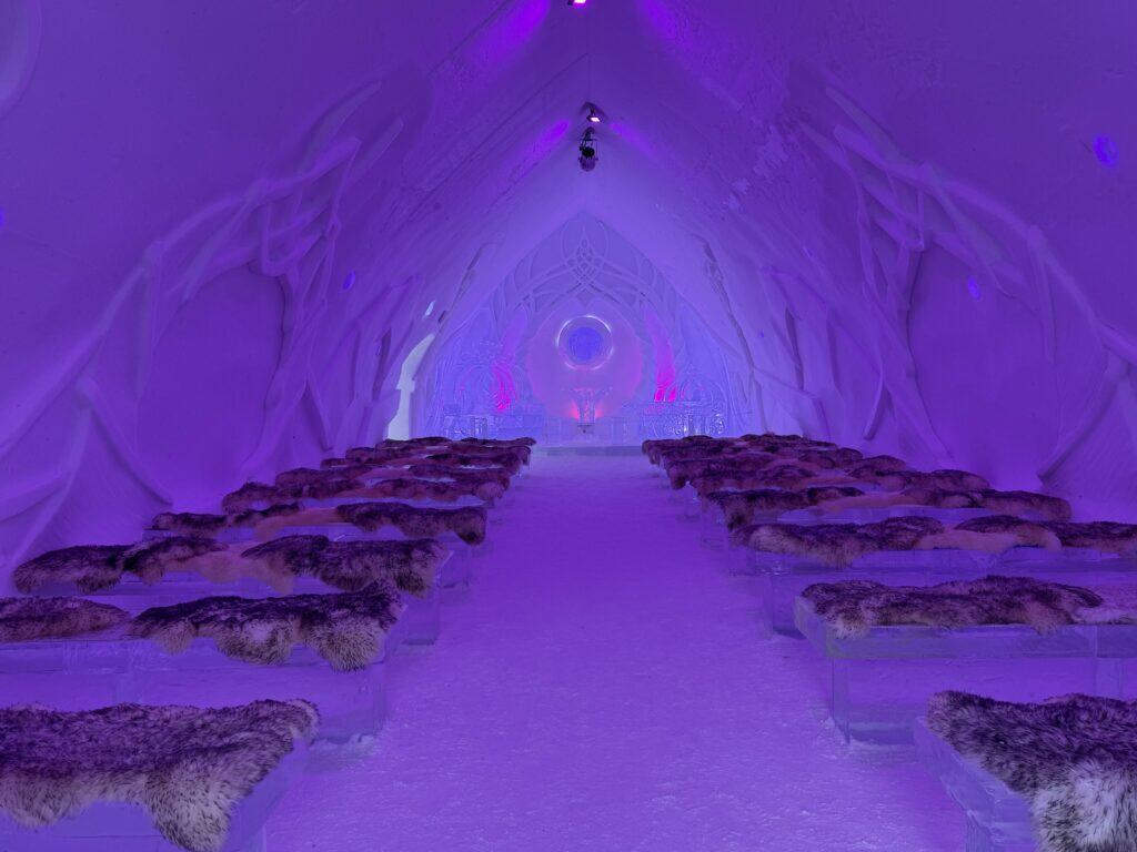 chapel at the ice hotel in quebec with furs on ice benches - altar made of ice - purple lighting.