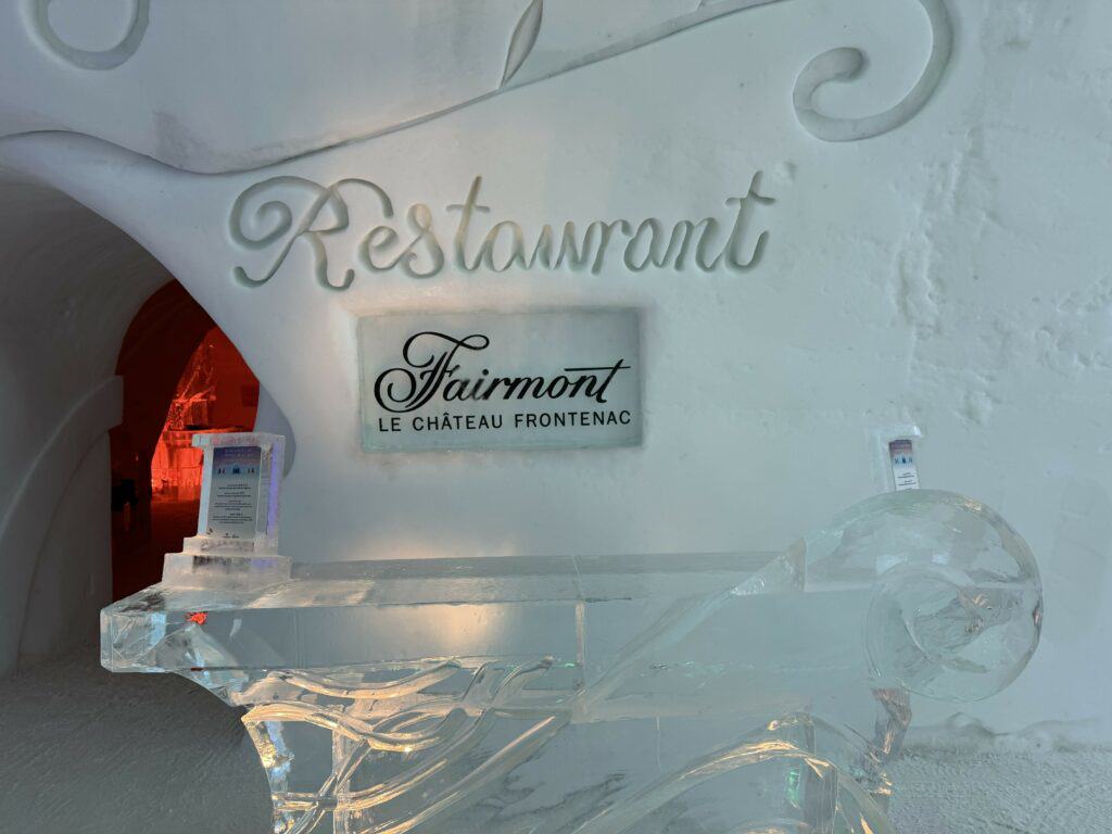 desk made of ice at entrance with the word 'Restaurant' engraved in cursive in the snow above sign reading "Fairmont Le Chateau Frontenac".