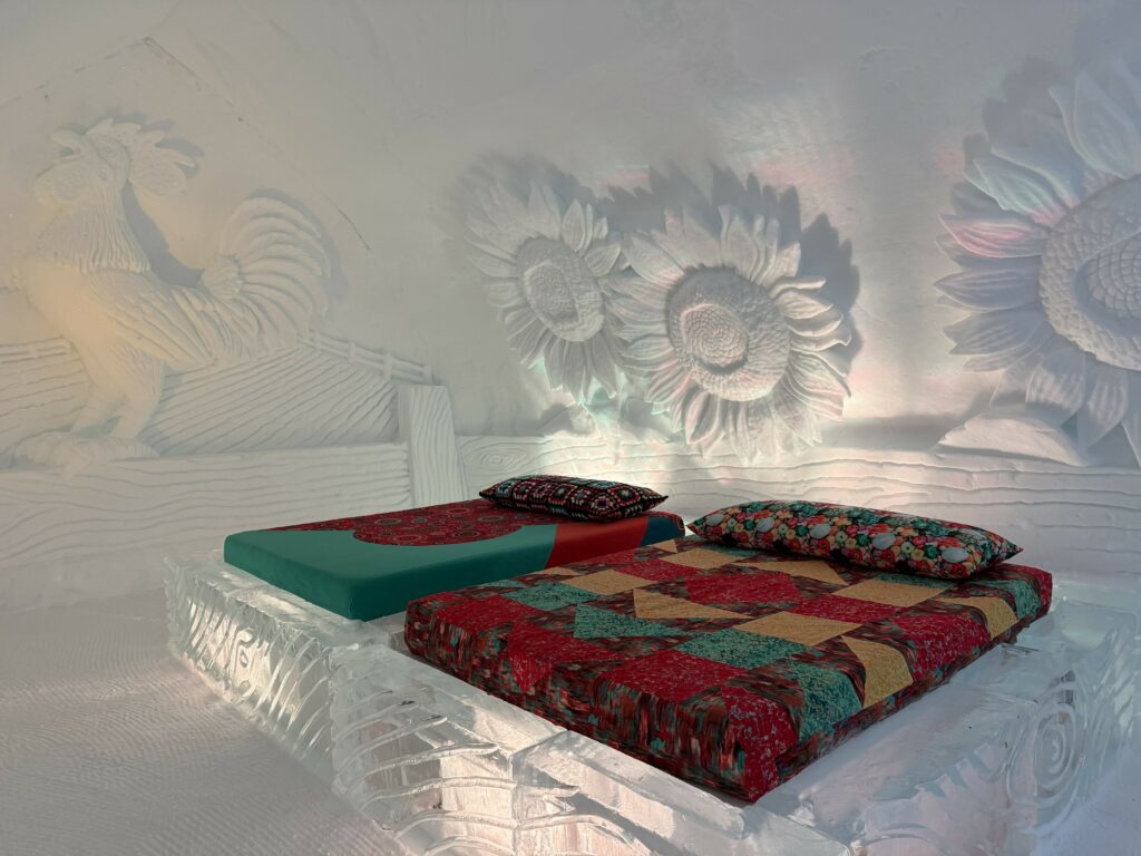 quebec city ice hotel - two ice beds with colourful red, green, and yellow bedding with a rooster and sunflowers carved in the walls.