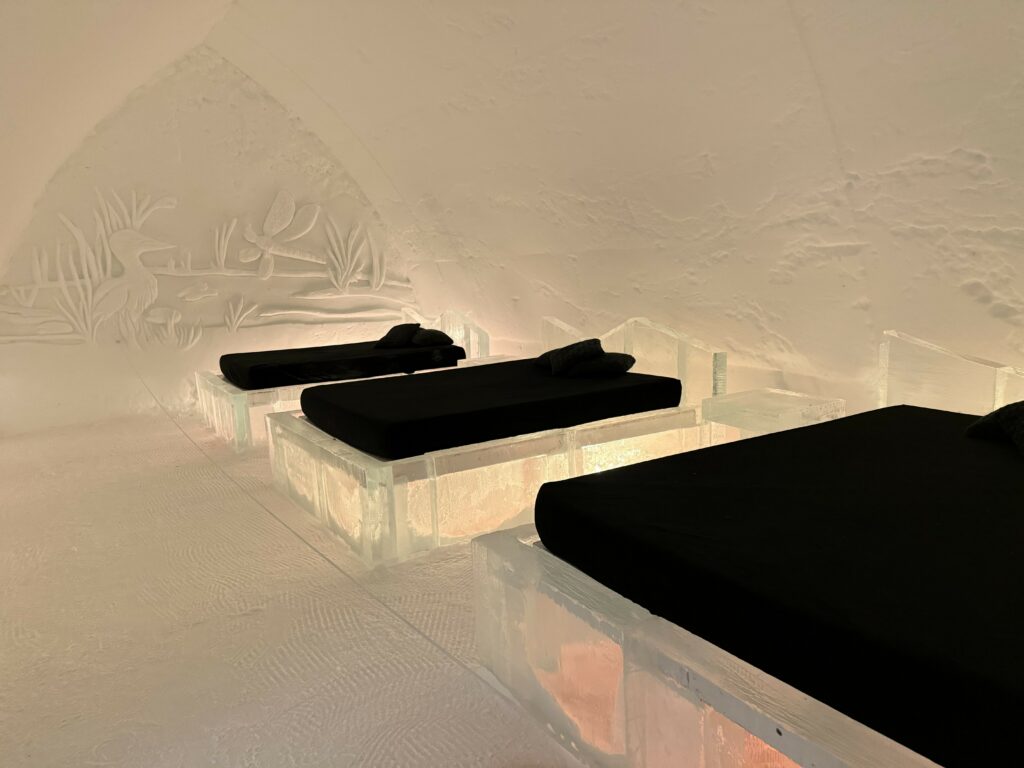 room with three ice beds with dark coverings at quebec ice hotel - wall covering in snow wall.