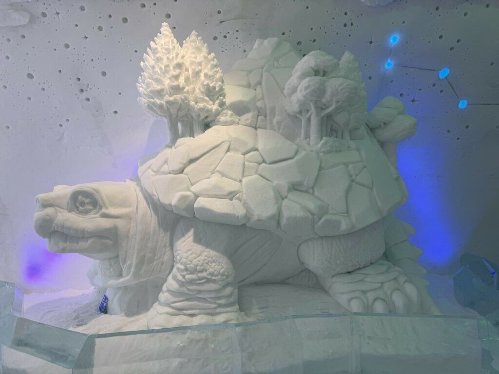 large snow sculpture of tortoise with small trees on back at quebec city ice hotel.