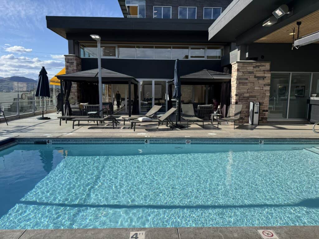 rectangle rooftop pool with light blue lining - lounge chairs and cabanas around pool.