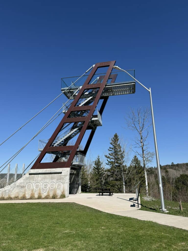 dark metal tower with concrete base and stairs and word "nipigon" inscribed in base with bright blue sky.