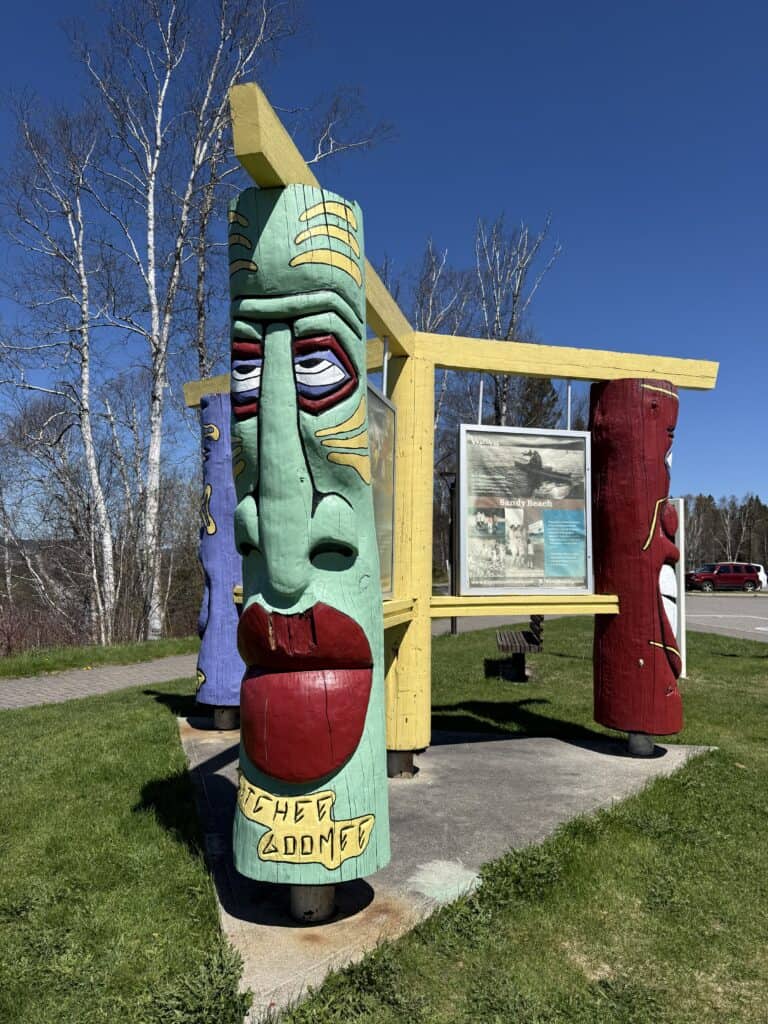 information board outside the Wawa Visitor Centre with three colourful wooden totem-like structures painted with faces.
