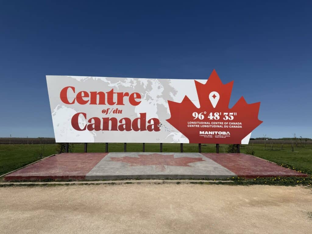 large red and white Centre of/du Canada sign with red maple leaf and geographic coordinates.