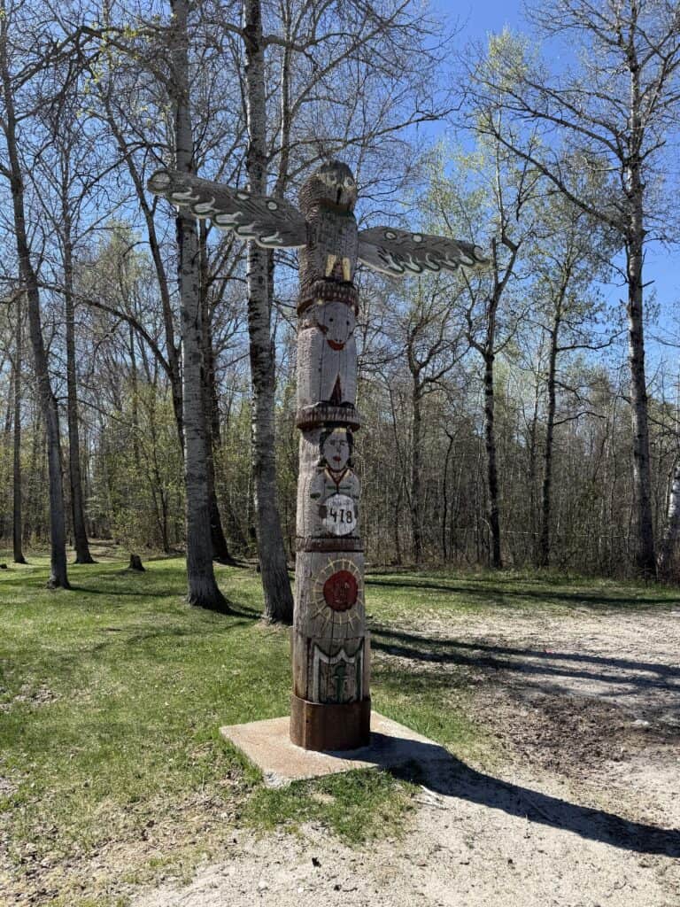 small totem pole in front of wooded area outside the Ignace Visitor Information Centre.