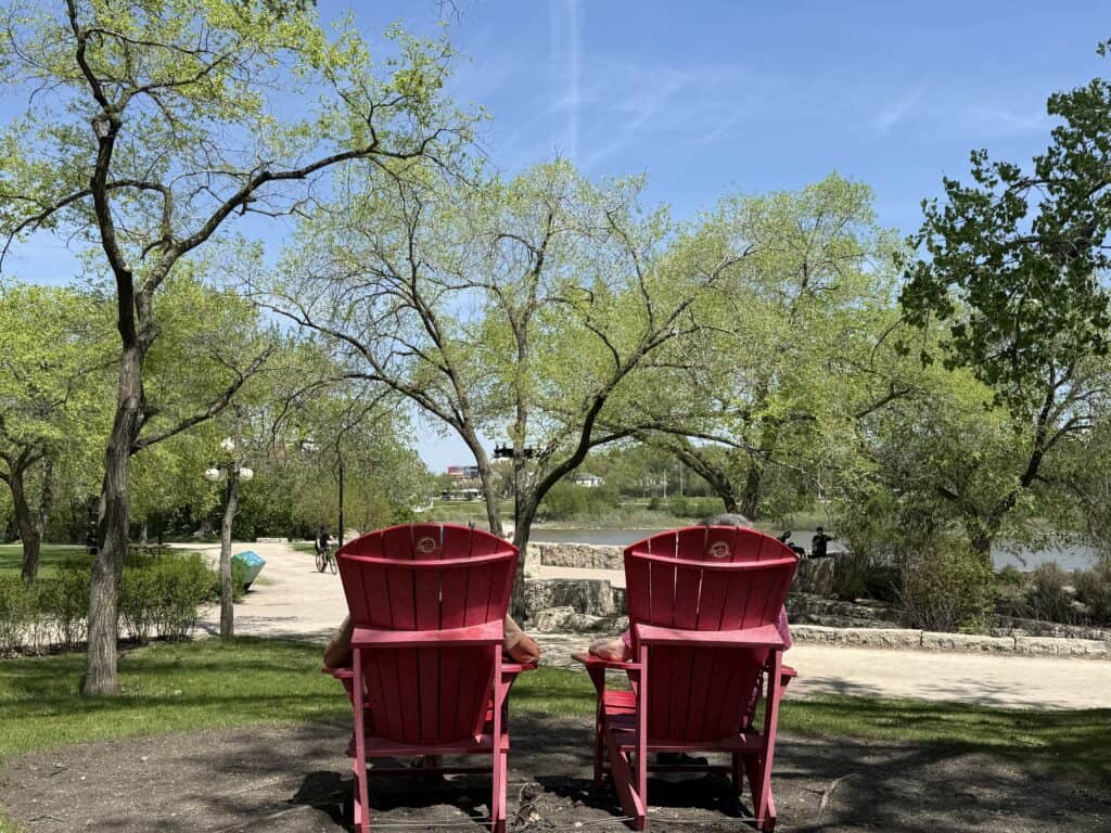 two red Parks Canada chairs at The Forks National Historic site by the river in Winnipeg
