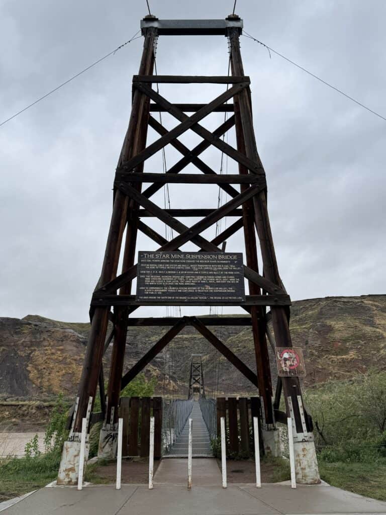 large metal suspension bridge with badland hills in background in Drumheller.